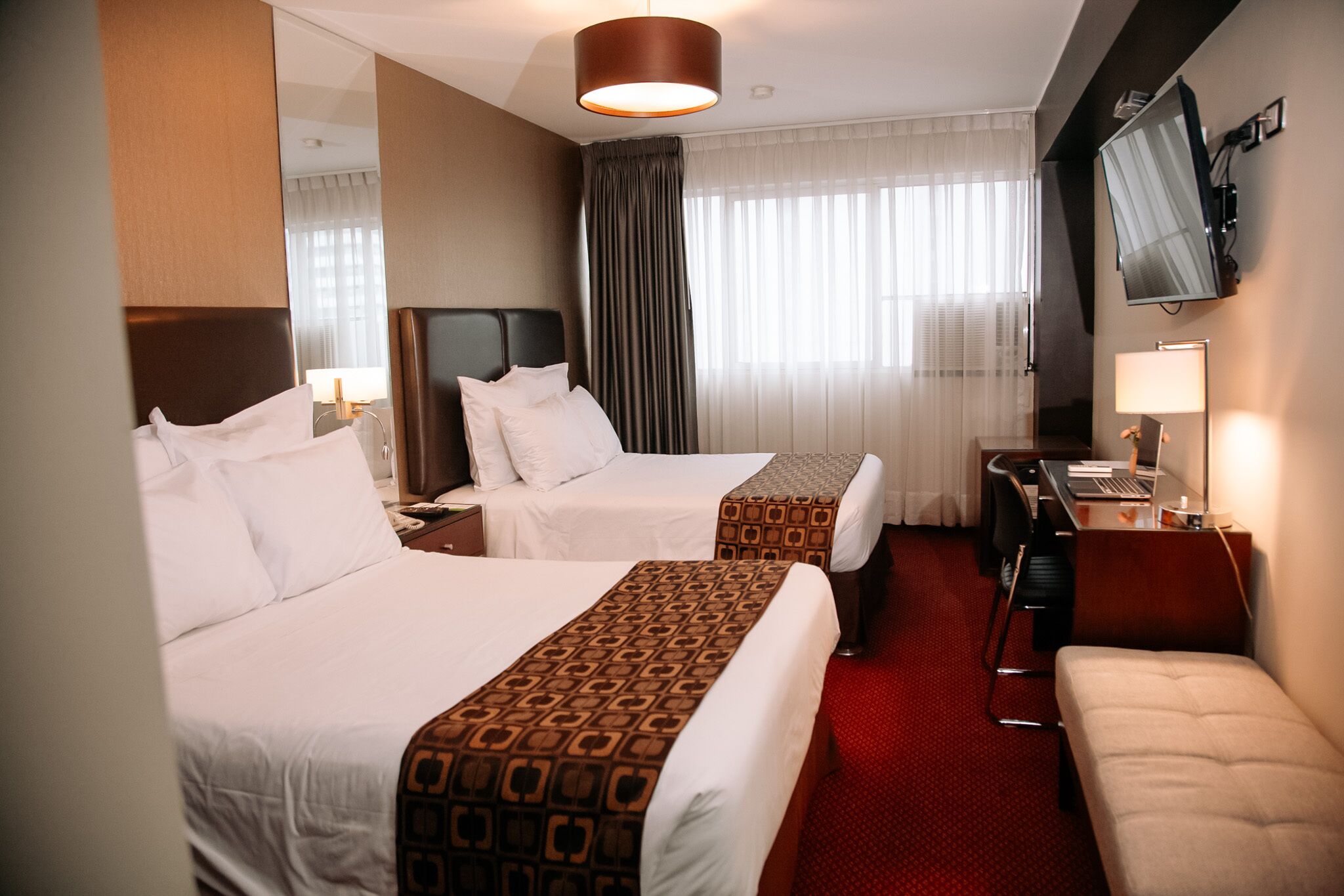 A hotel room with two beds, a desk with a computer, a chair, and a TV mounted on the wall.