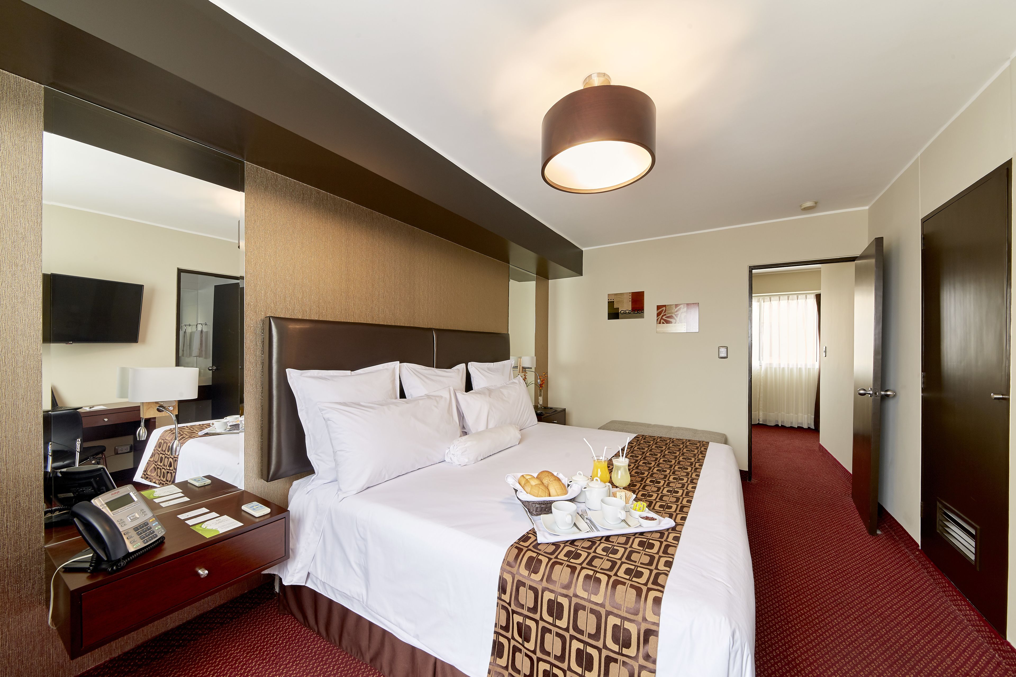 A hotel room with a large bed, a desk with a telephone, a mirror, and a breakfast tray on the bed.