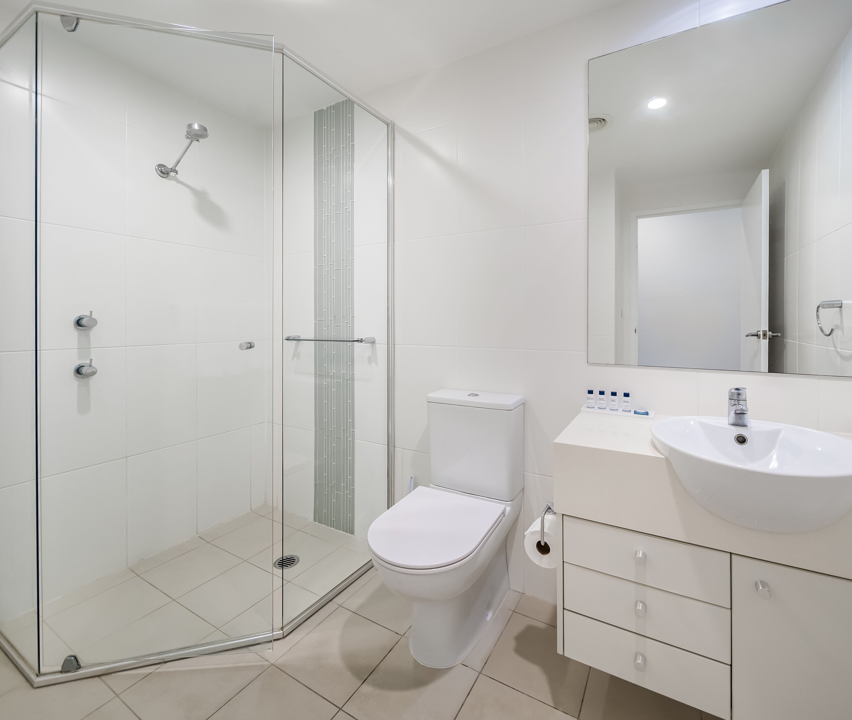 A modern bathroom with a glass shower enclosure, a white toilet, and a vanity with a sink and mirror.