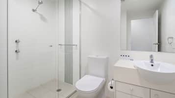 A modern bathroom with a glass shower enclosure, a white toilet, and a vanity with a sink and mirror.