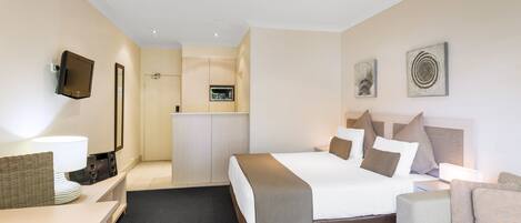 A hotel room with a bed, a sofa, a desk, a TV, and a kitchenette.