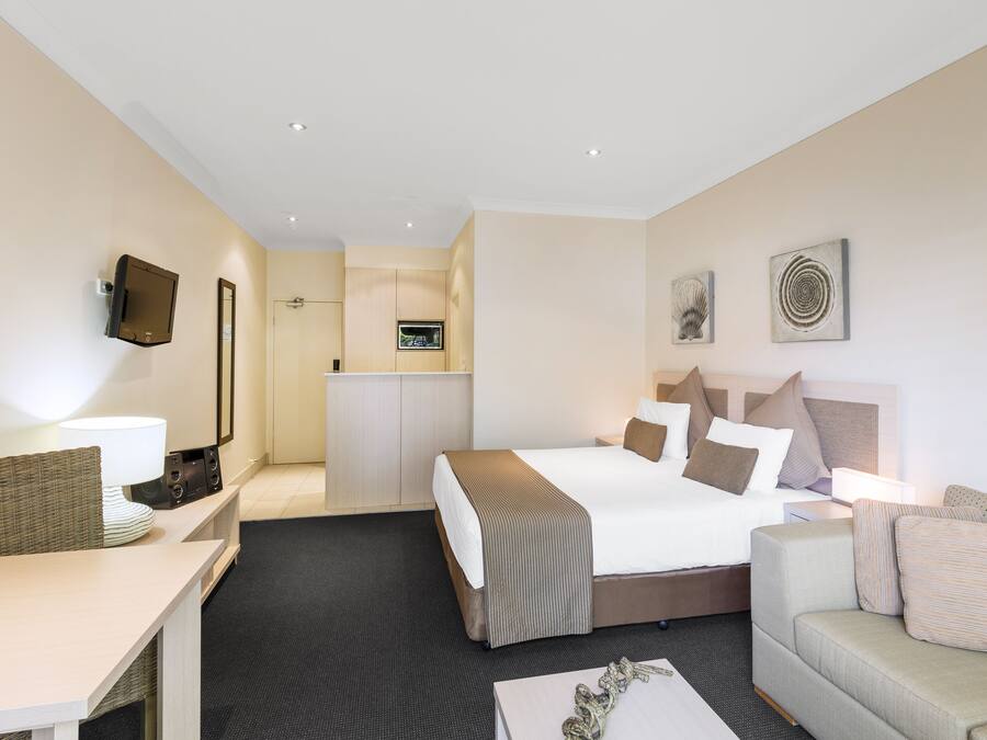 A hotel room with a bed, a sofa, a desk, a TV, and a kitchenette.