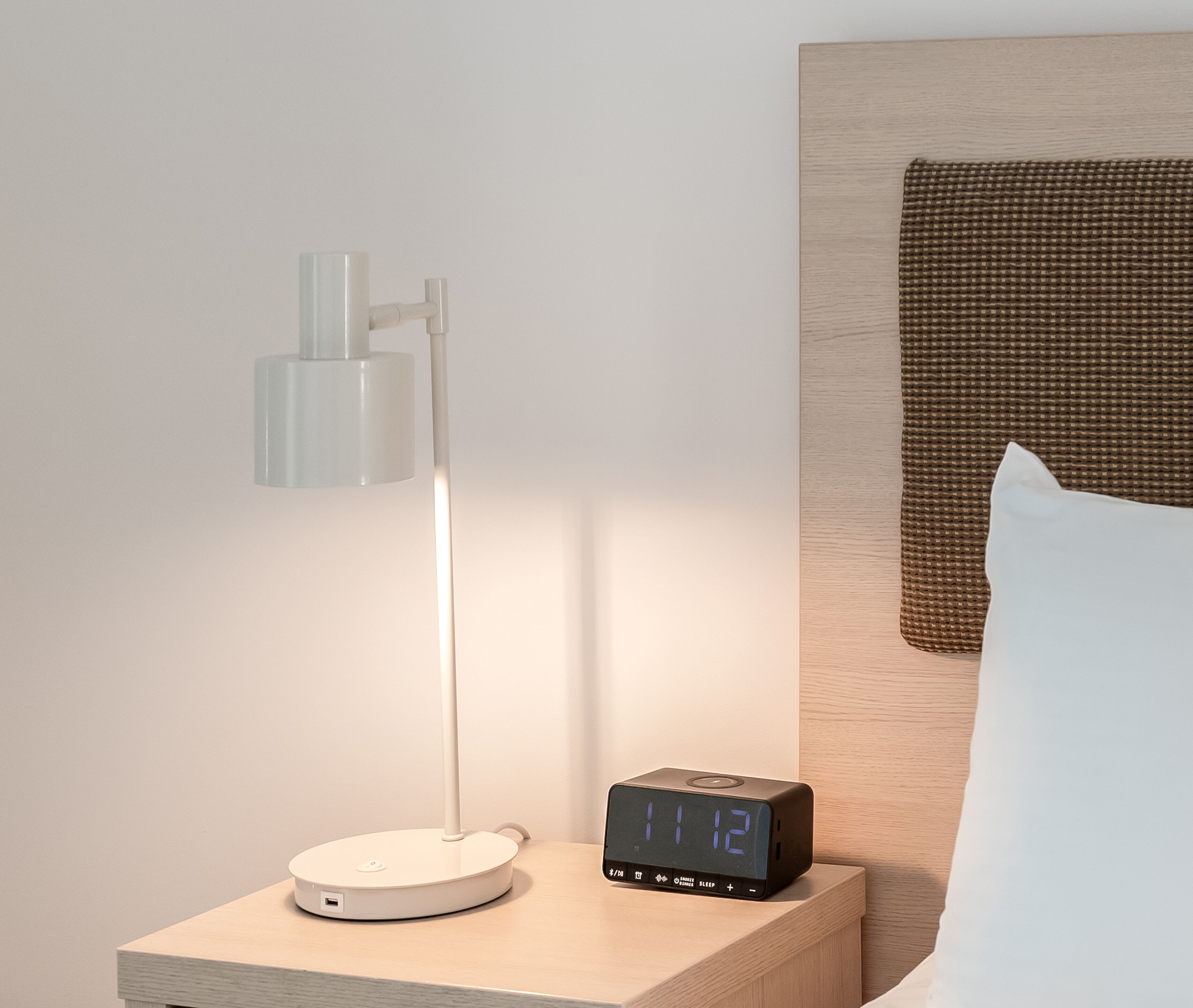 A bedside table with a modern lamp and a digital clock displaying the time.