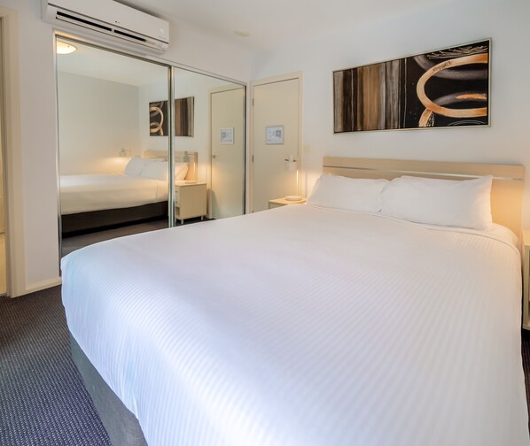 A hotel room with a large bed, a bedside table, a nightstand, a mirror, a wall-mounted artwork, and a wardrobe.