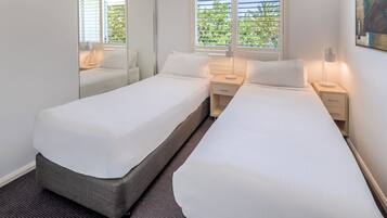 Habitación de hotel con dos camas individuales, un espejo grande, una ventana con persianas y un cuadro en la pared.