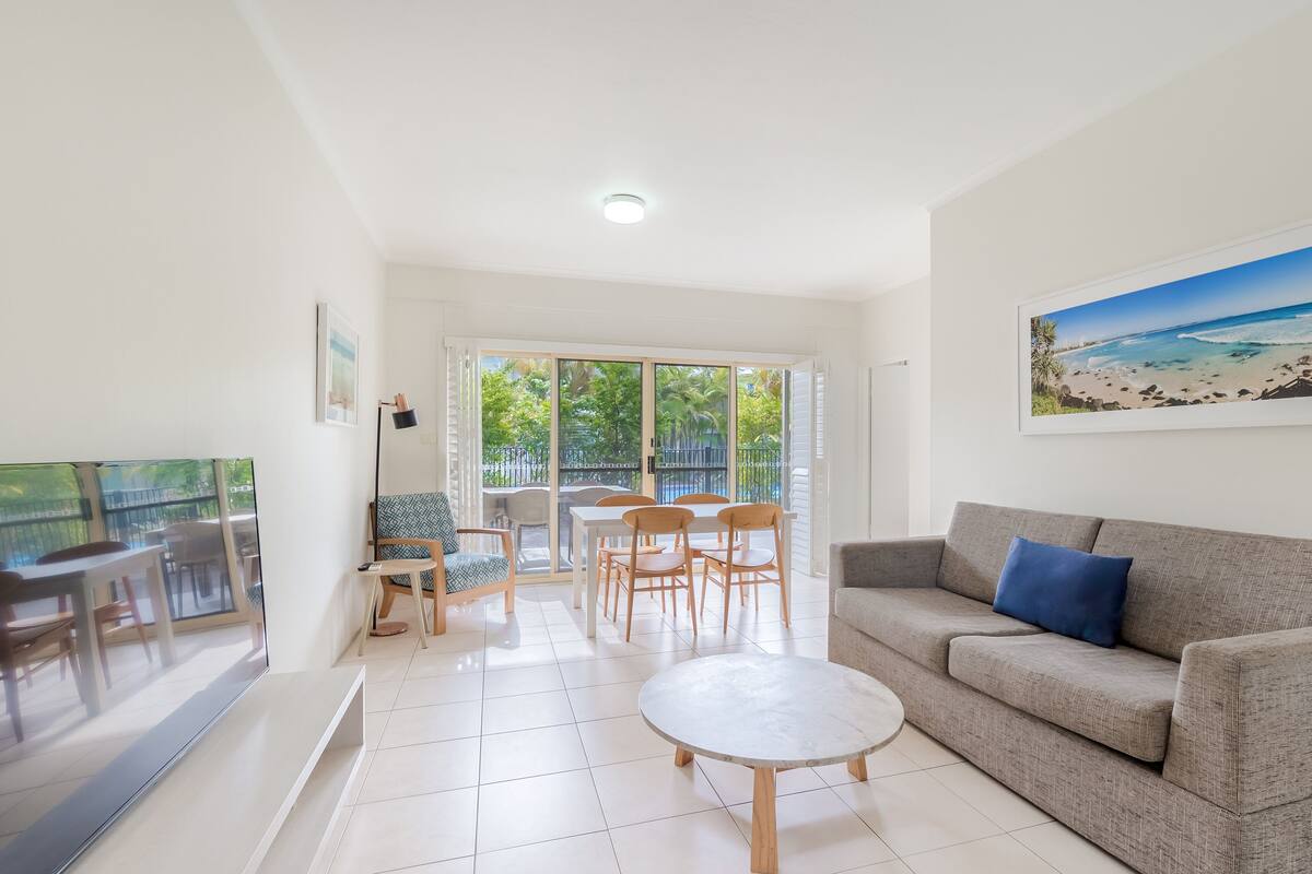 A modern living room with a grey sofa, a round coffee table, and a dining area with wooden chairs and a white table.