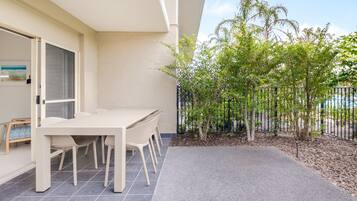 Un patio con mesa y sillas, un pequeño jardín con árboles, y vista al cielo.