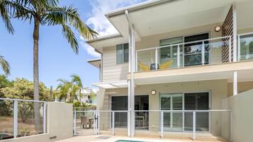 En moderne bygning med to etager, en swimmingpool, store vinduer og en balkon med en gul stol.
