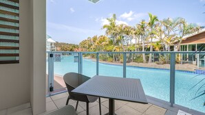 A balcony with a pool view, a table, and chairs.