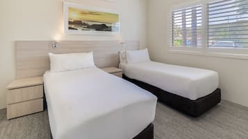 A hotel room with two beds, a nightstand, a wall-mounted air conditioner, a framed picture, and a window with blinds.