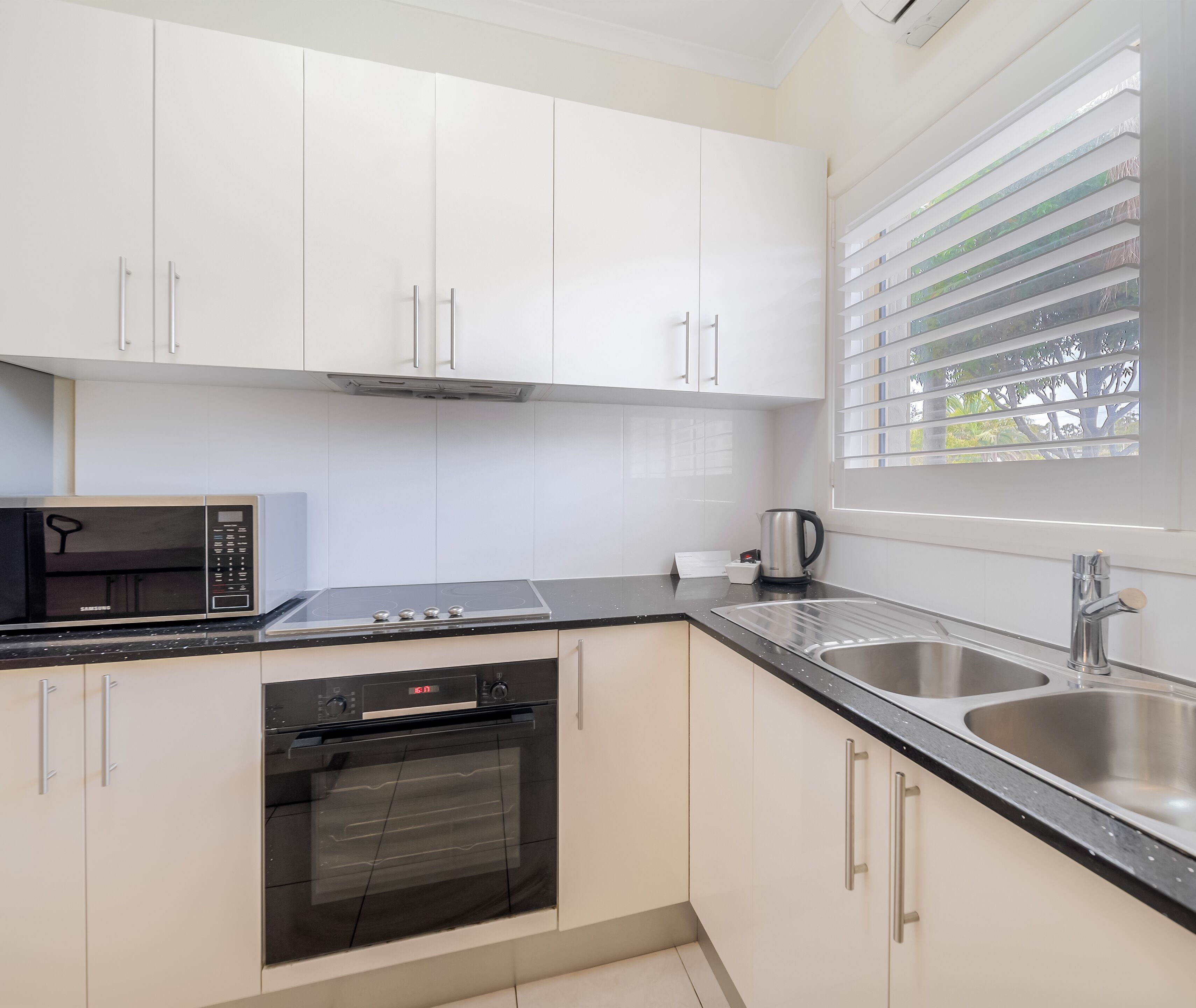 A modern kitchen with white cabinets, a black microwave, a stove, an oven, and a sink.