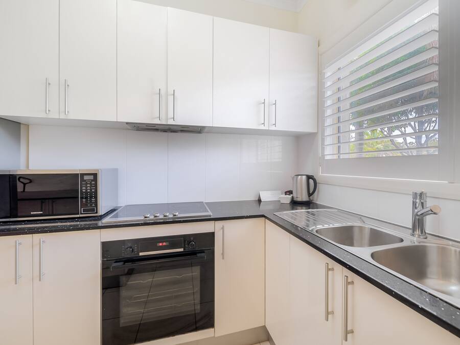 A modern kitchen with white cabinets, a black microwave, a stove, an oven, and a sink.