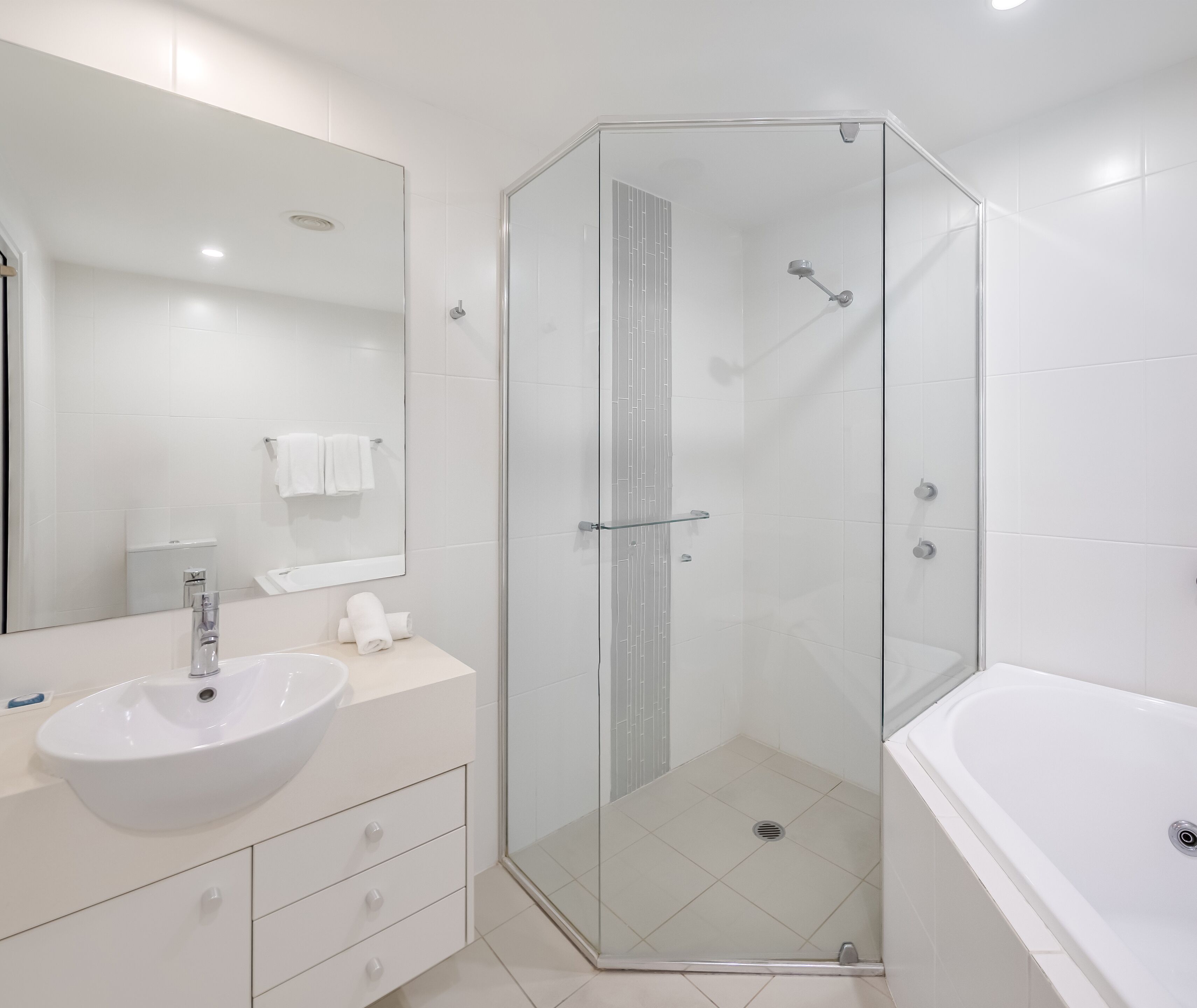 Un baño moderno con ducha envuelta en vidrio, un lavabo blanco y un espejo grande.