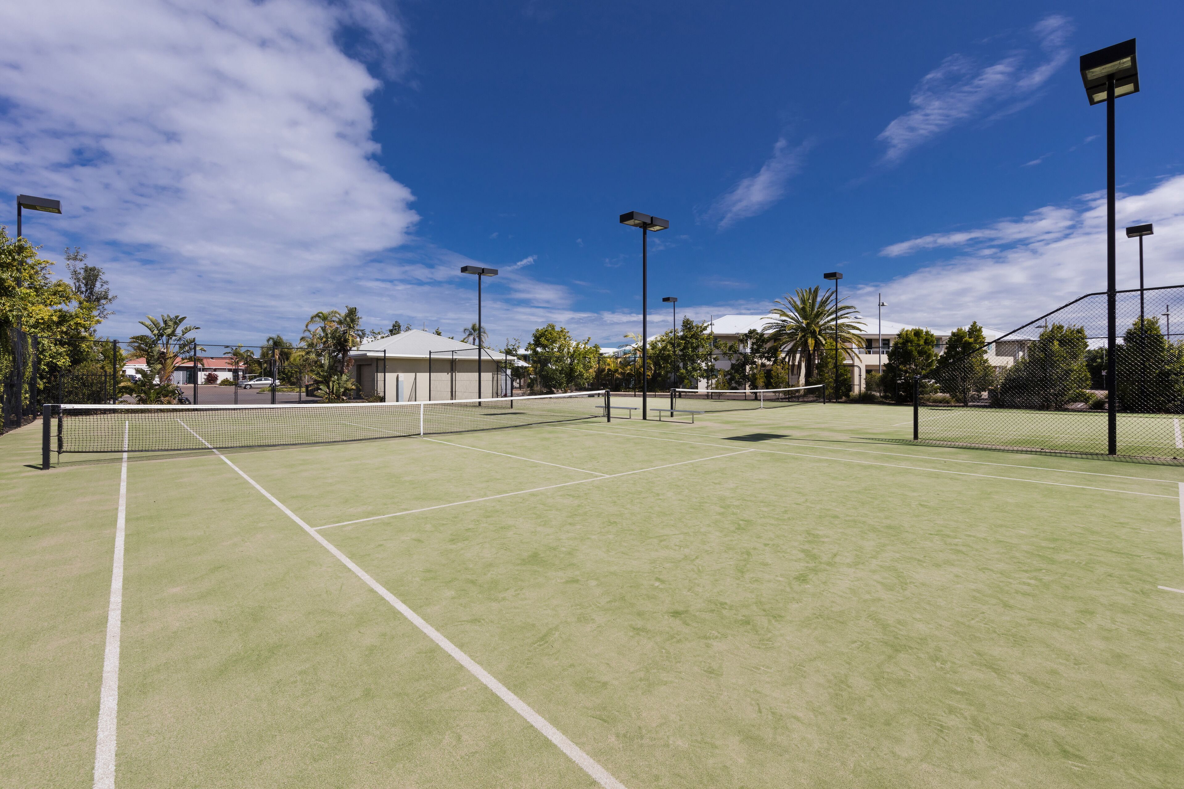 An outdoor tennis court with a net, surrounded by trees and buildings.