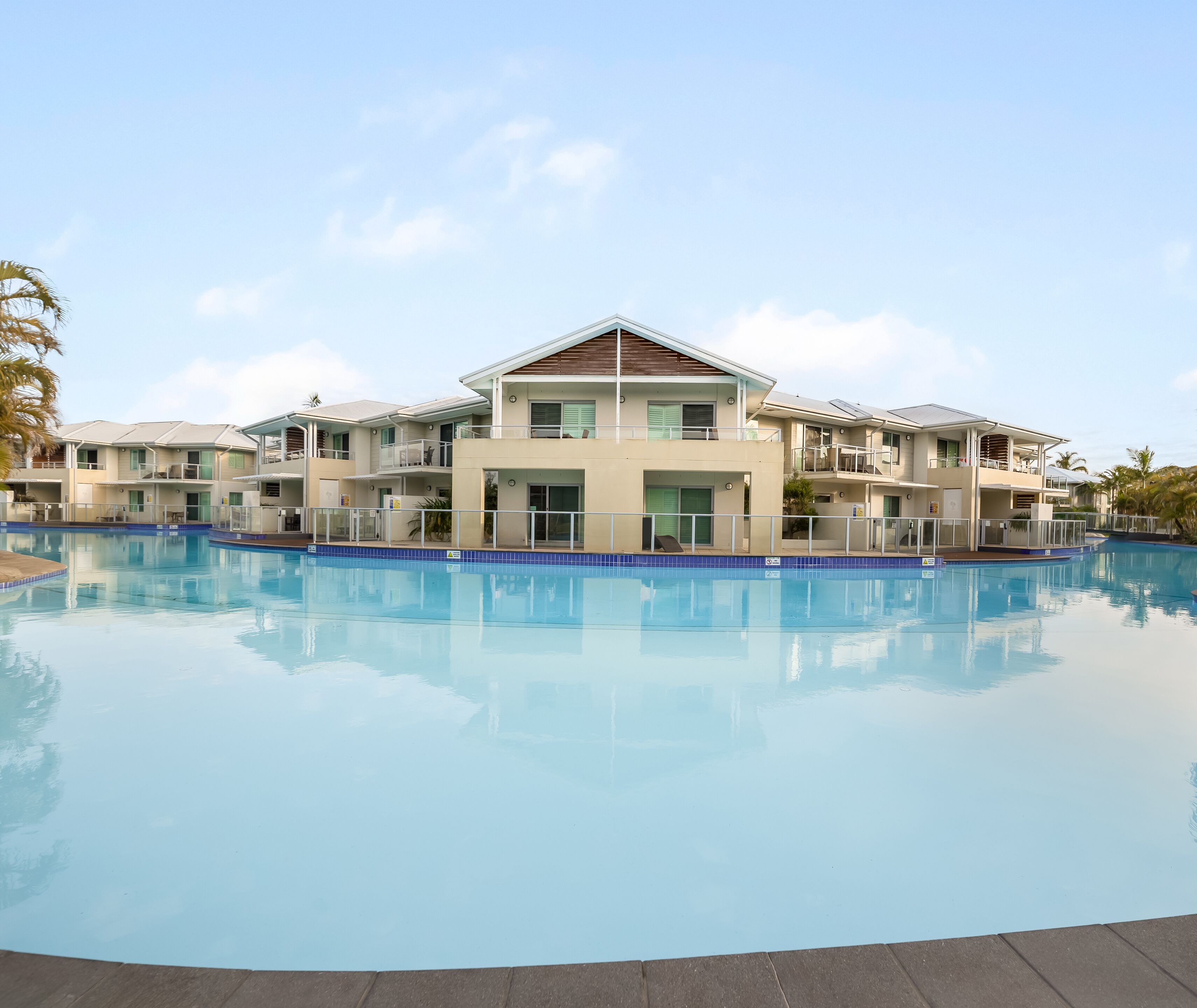 A hotel with a swimming pool, multiple balconies, and a clear sky.