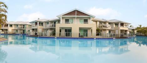 A hotel with a swimming pool, multiple balconies, and a clear sky.