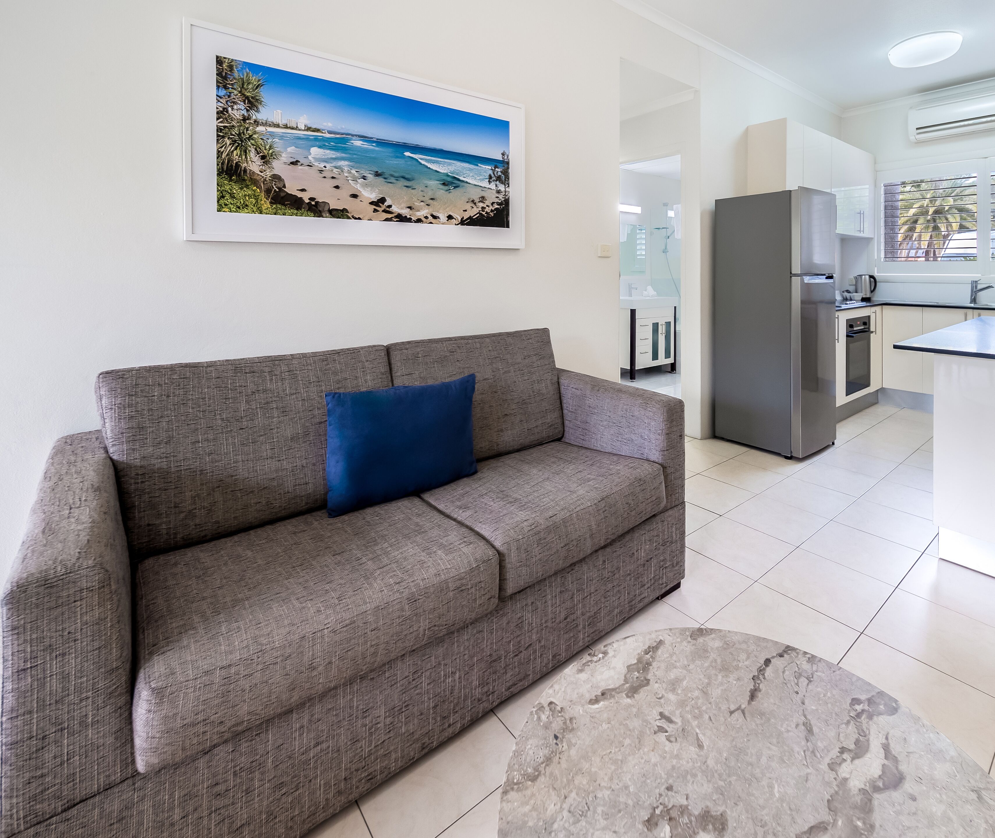A modern living room with a grey sofa, a blue cushion, and a large framed beach photograph on the wall.