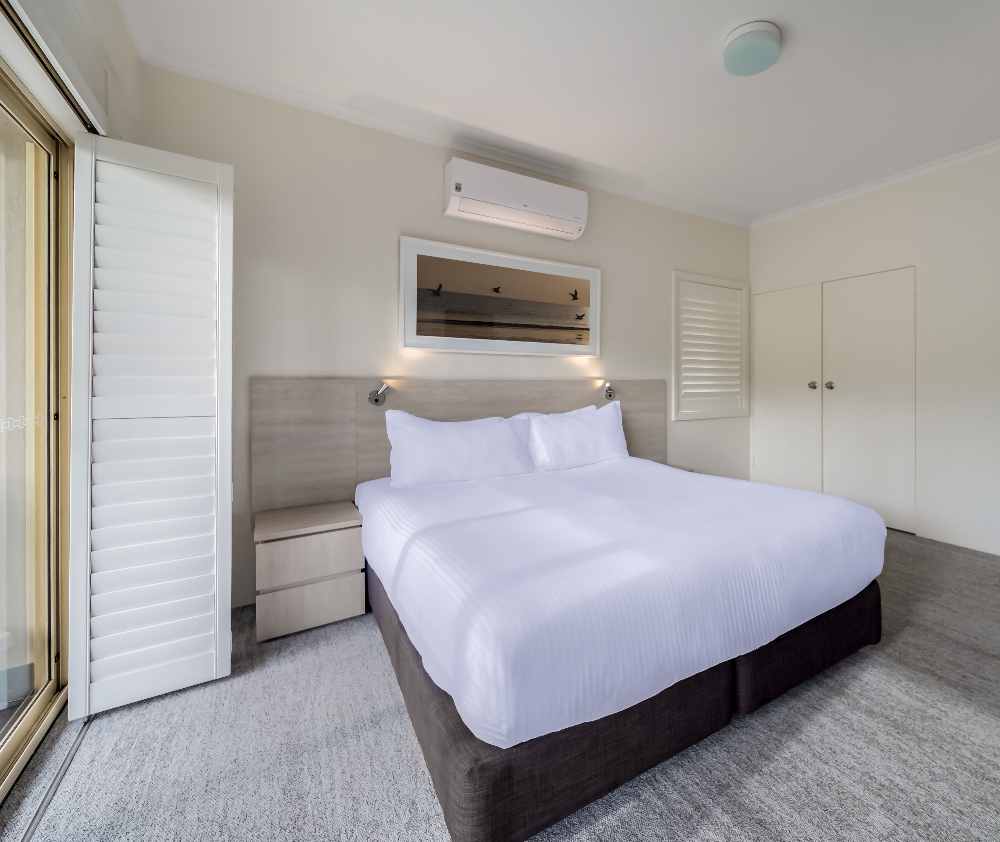 Habitació d'hotel amb un llit gran, una taula de nit, aire condicionat fixat a la paret i una porta amb vista a l'exterior.