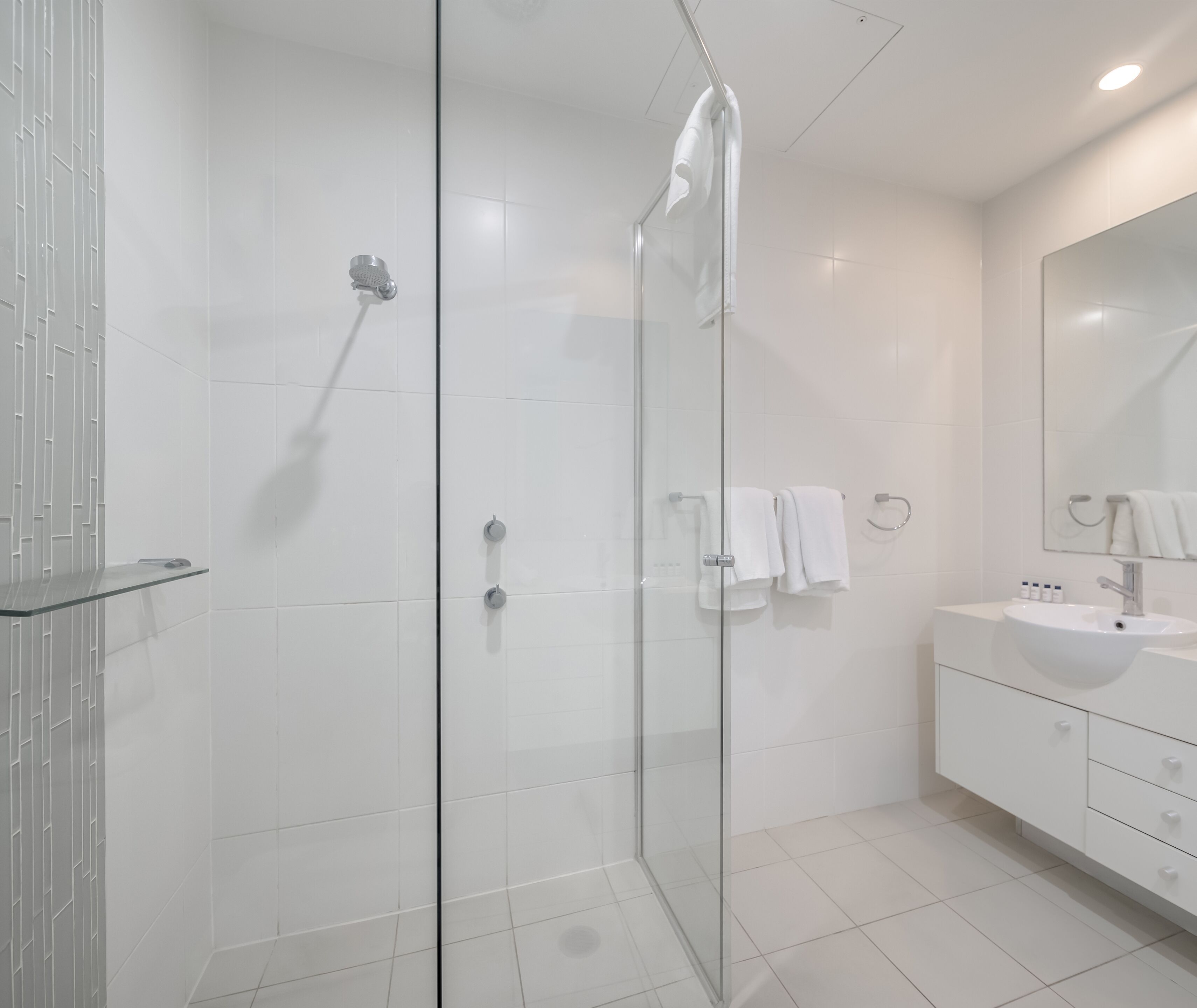 A modern bathroom with a glass shower enclosure, white tiled walls, and a vanity with a sink and mirror.