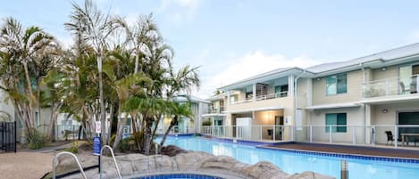 Un hôtel doté d’une piscine entourée de palmiers et bordée de rochers.