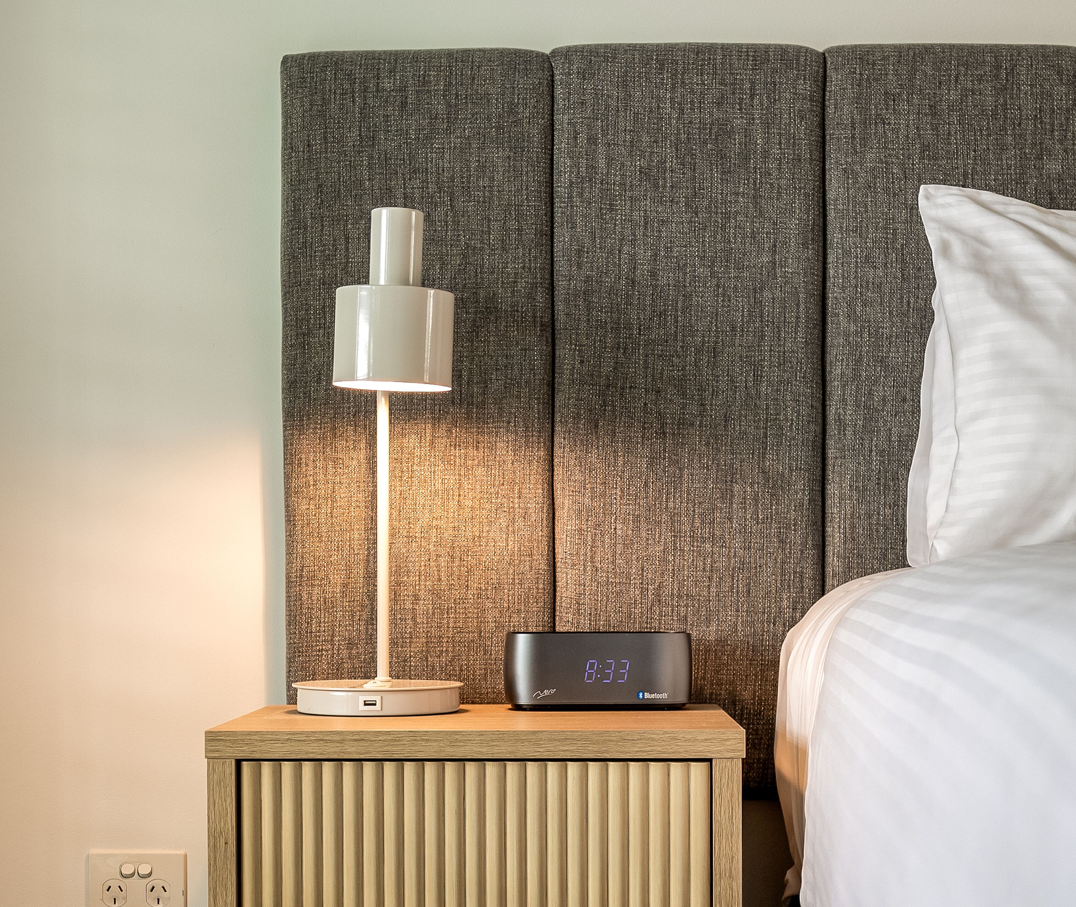 A bedside table with a lamp and a digital clock displaying the time.