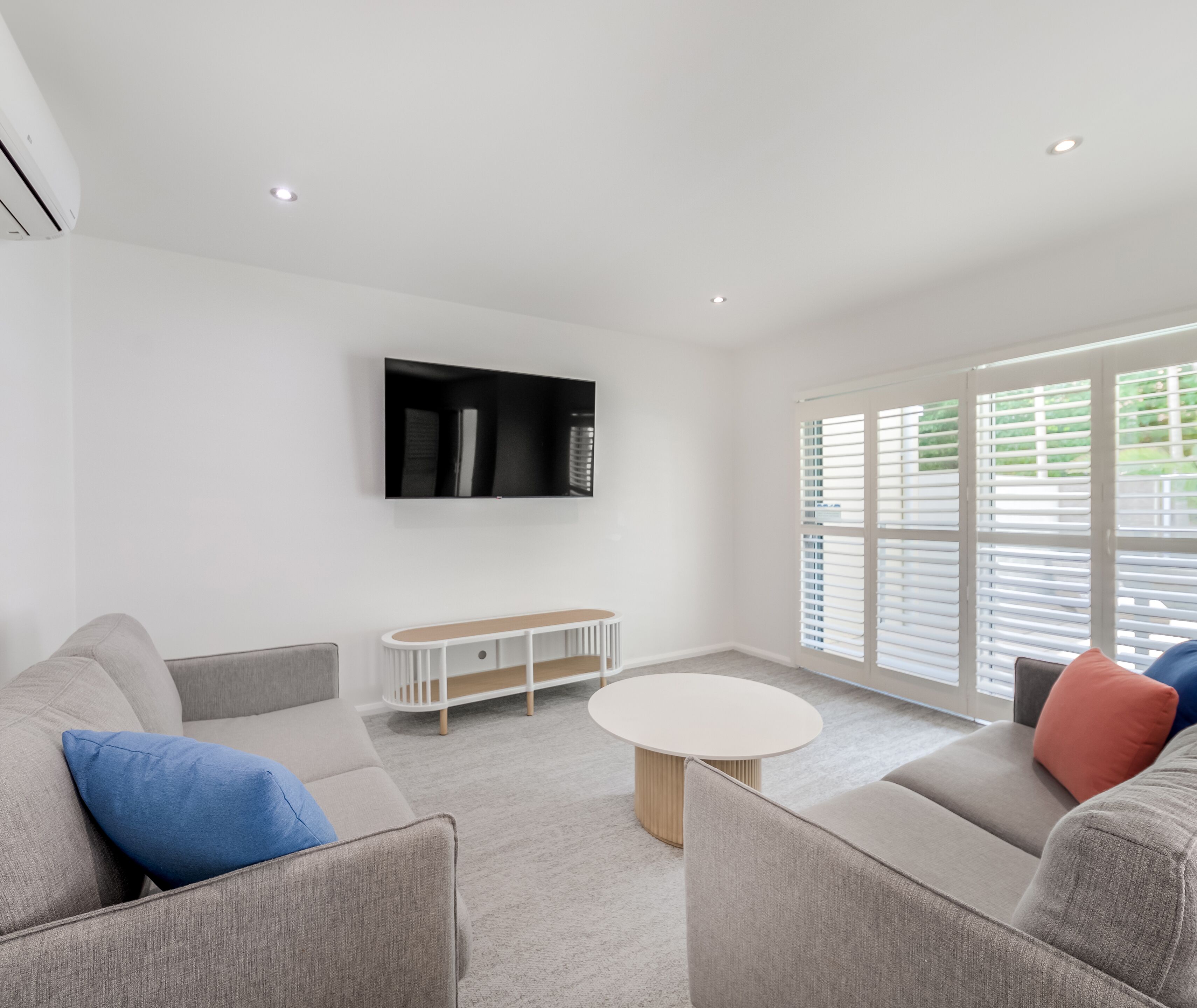 A modern living room with a flat-screen TV mounted on the wall, a round coffee table, and a sofa with cushions.