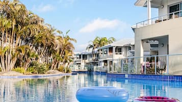 Una piscina con dos flotadores, rodeada de palmeras y edificios modernos.