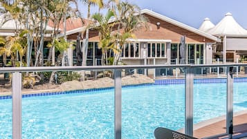 A swimming pool with a clear blue water surface, surrounded by a metal railing, and a view of a building with large windows and a tiled roof.