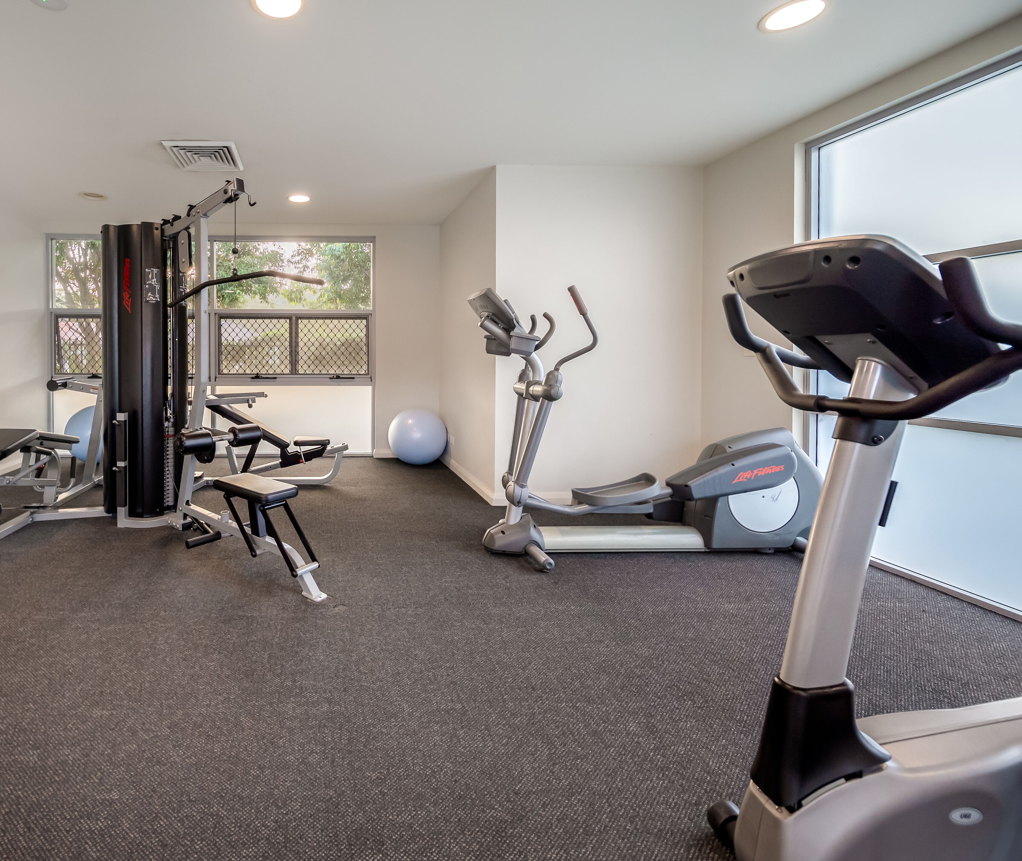 Un gimnasio con equipo de cardio, máquinas de pesas y una pelota grande para ejercicios.