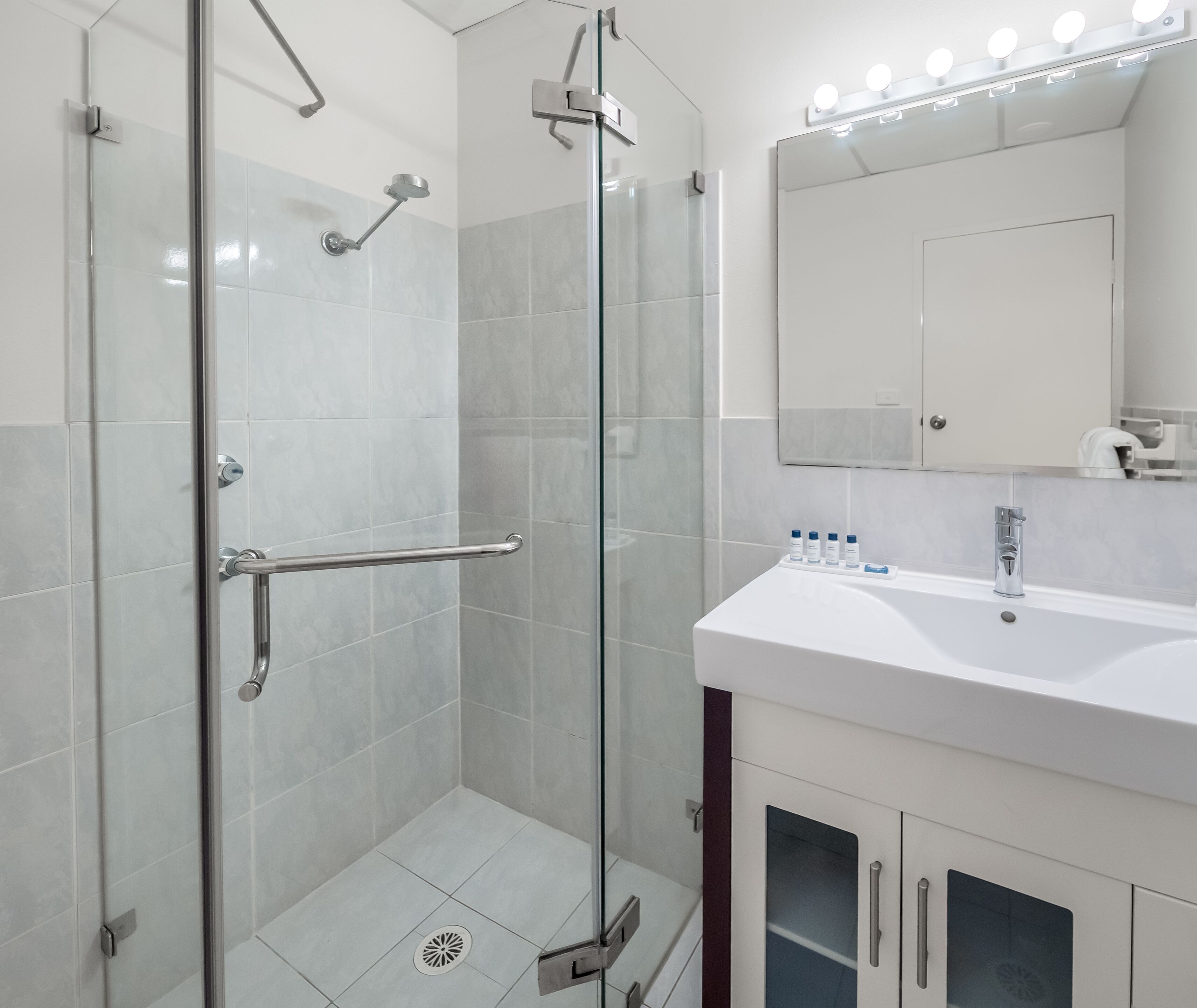 Une salle de bain moderne avec une douche en verre, un lavabo blanc et un miroir avec des lumières au-dessus.