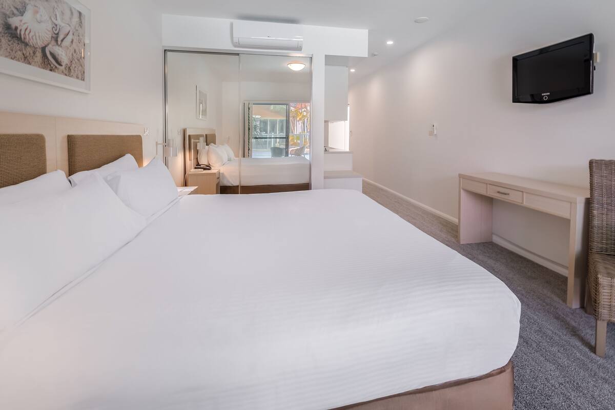 A hotel room with a large bed, a desk, a television, and a view of the outside.