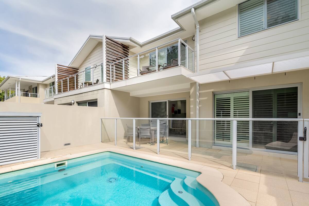 A modern two-story house with a swimming pool, a covered patio, and a balcony with outdoor furniture.