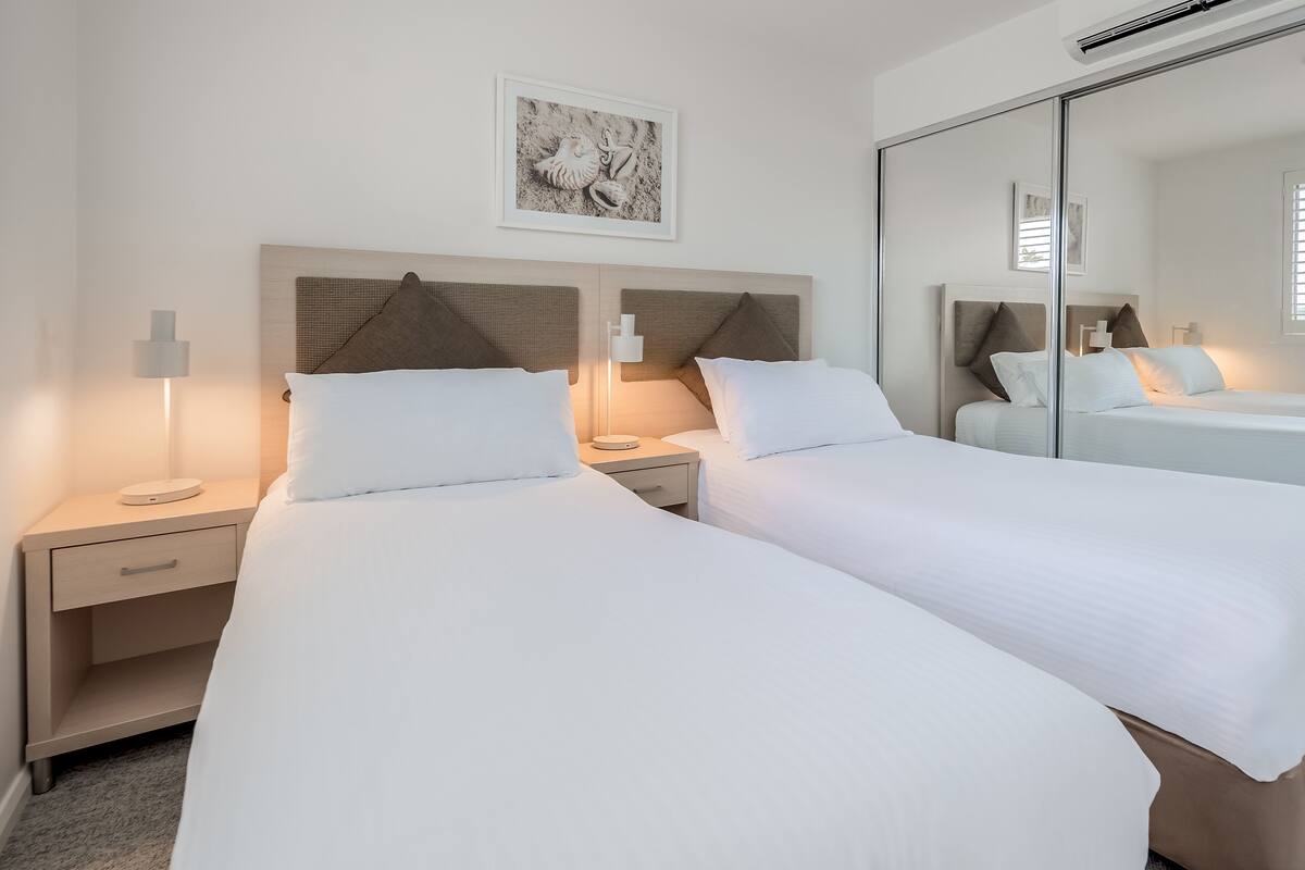A hotel room with two beds, a large mirror, and a framed picture on the wall.