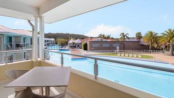 A balcony with a pool view, outdoor seating, and a clear sky.