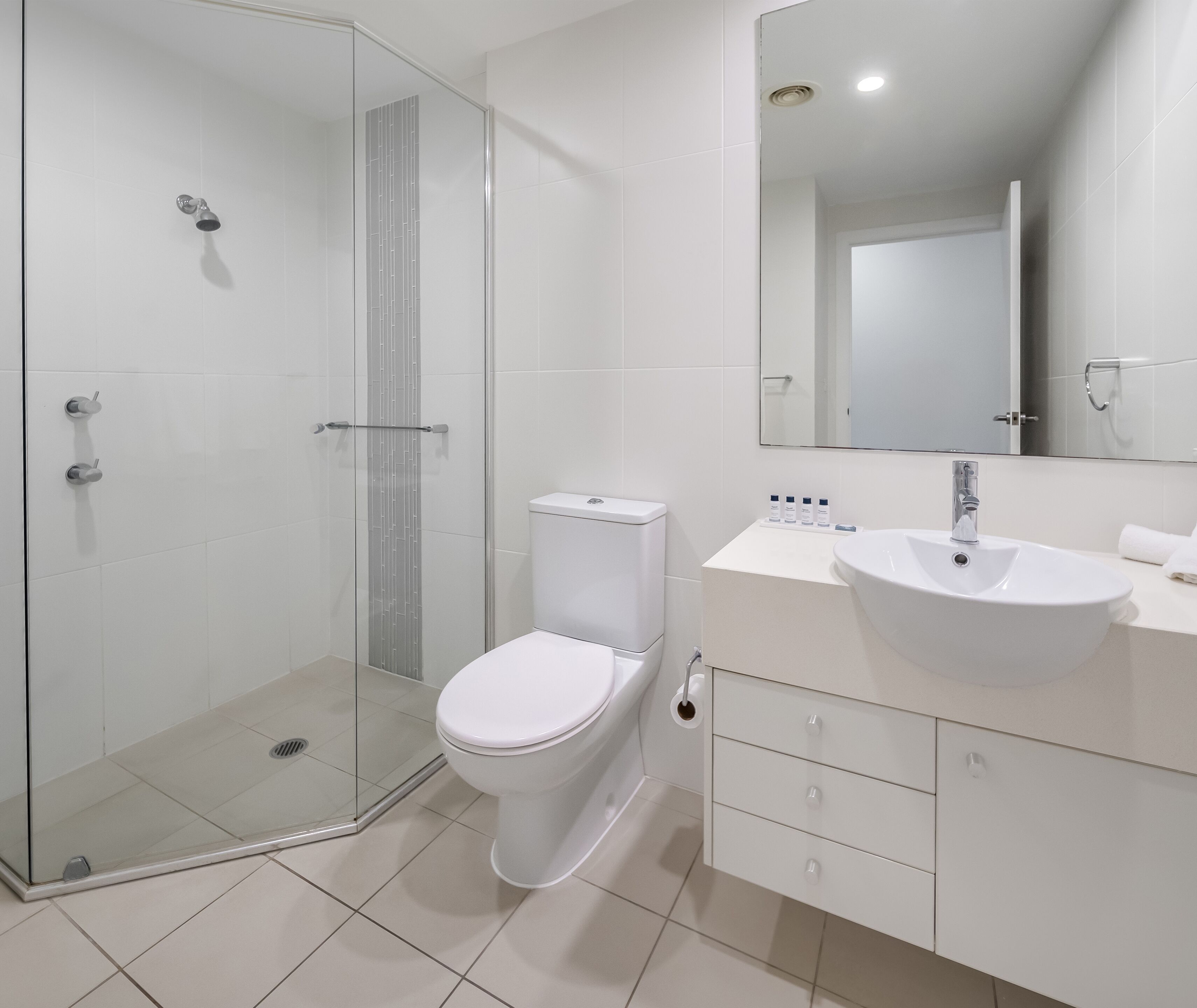 A modern bathroom with a glass-enclosed shower, a white toilet, and a vanity with a sink and mirror.