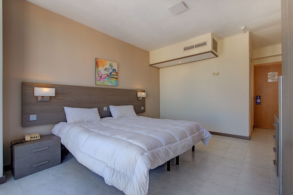 Habitación de hotel con una cama grande, mesitas de noche, un climatizador de pared y una puerta.