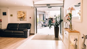 A hotel lobby with a black leather sofa, a large potted plant, and a zebra sculpture on a white console table. - Hotel Primera (St. Paul's Bay)