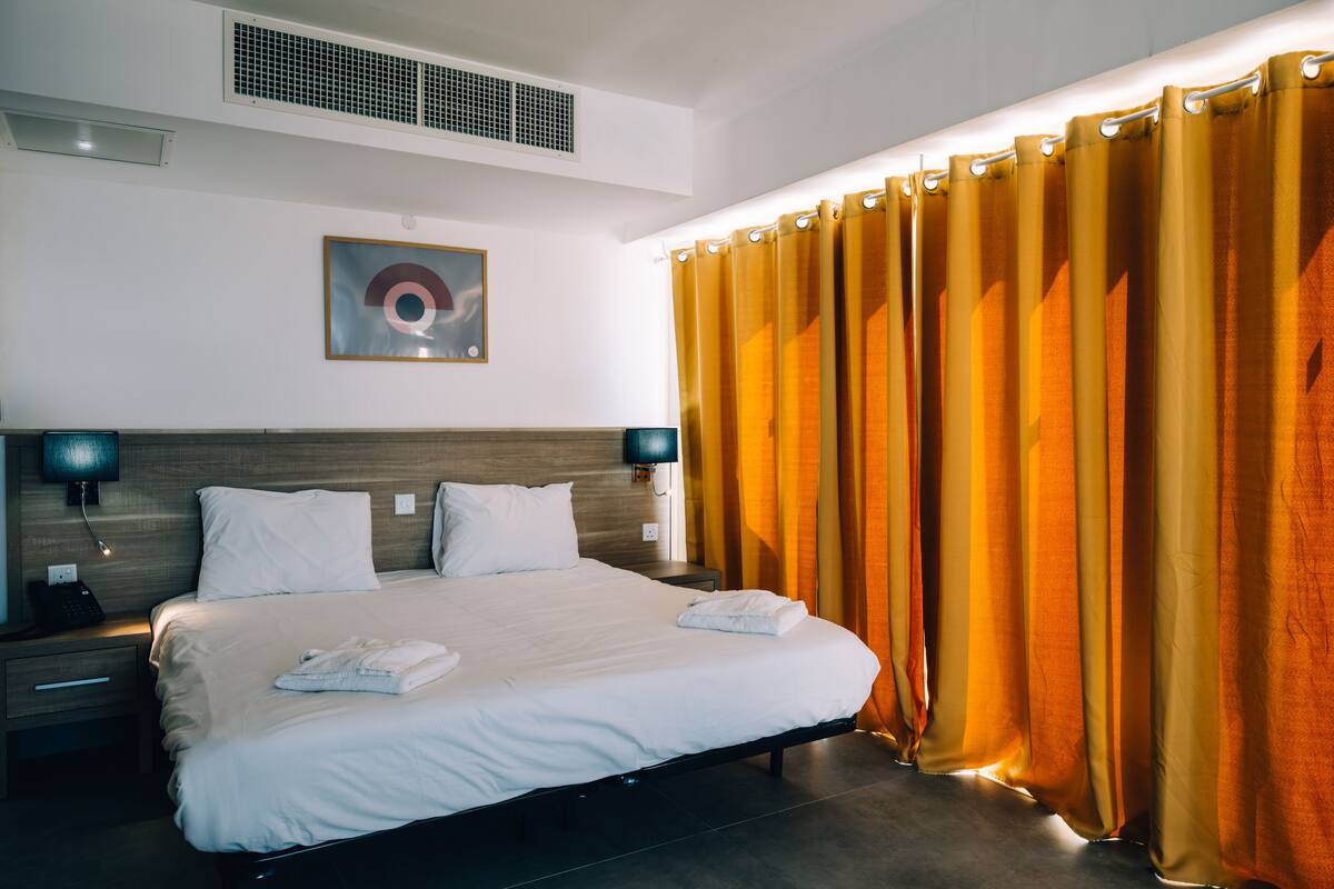 A hotel room with a large bed, two bedside tables, a wall-mounted phone, and a painting.