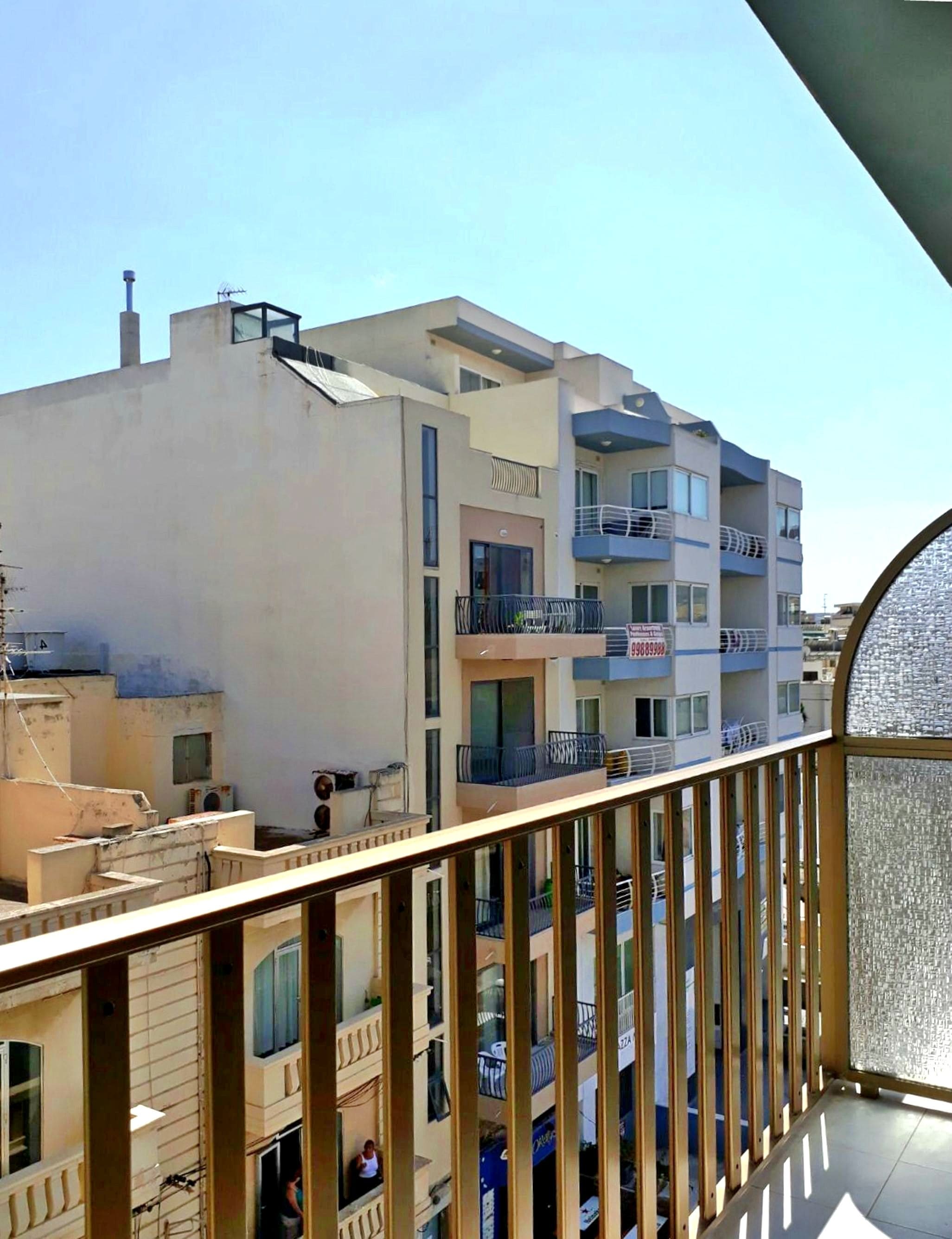 Un edificio de varios pisos con balcones, cielo despejado y vistas del entorno.