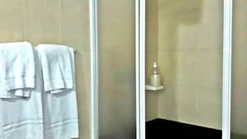 Un bagno con doccia vetrata, pareti rivestite di piastrelle color beige e due asciugamani bianchi appesi al muro.
