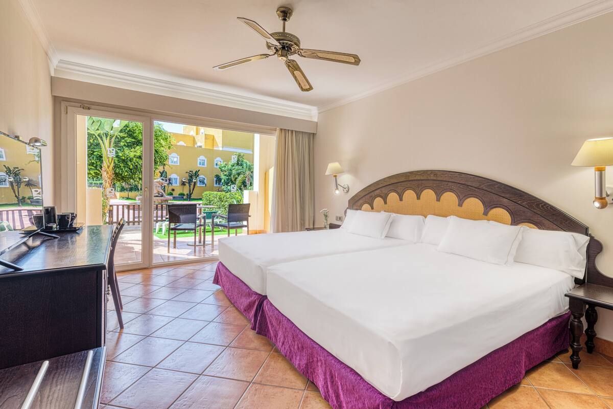 A hotel room with a large bed, a desk, a ceiling fan, and a view of the outside.