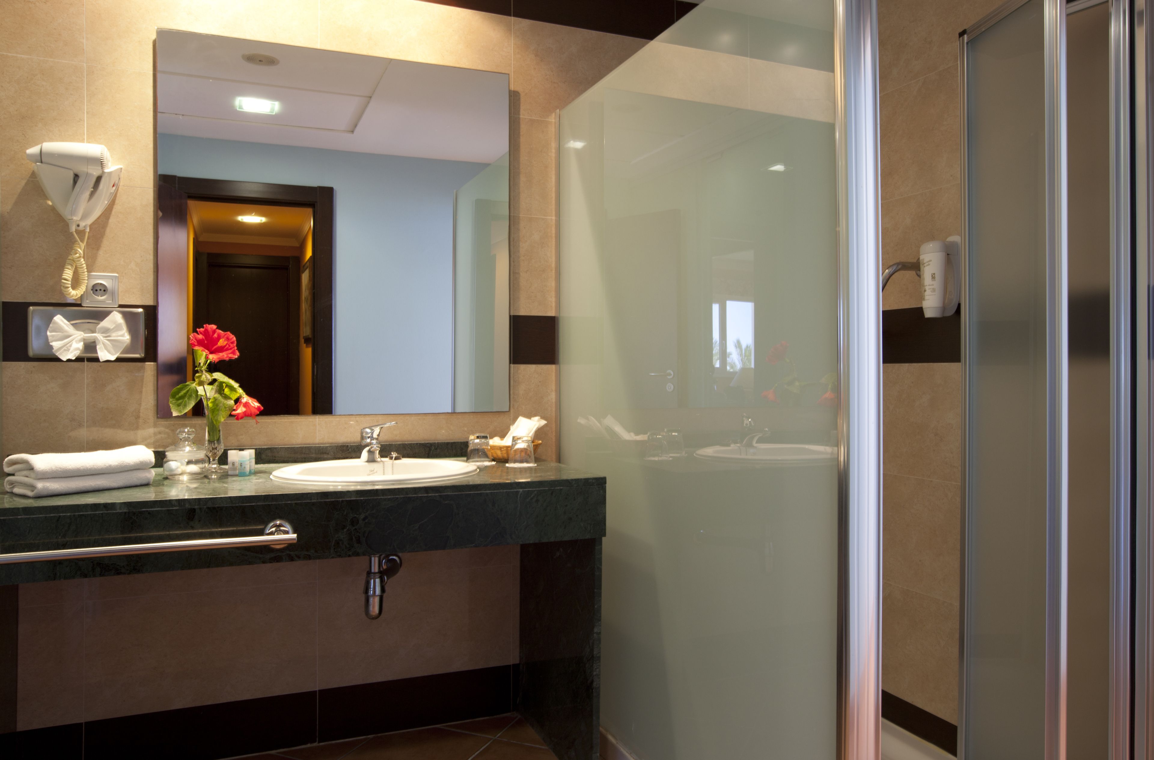 Un baño moderno con ducha de vidrio, lavamanos con toallero y espejo sobre el lavamanos.