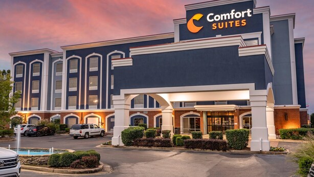 Un hotel con un gran letrero que dice 'Comfort Suites', que presenta un diseño arquitectónico moderno con una entrada destacada y un área de estacionamiento.
