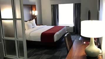 A hotel room with a bed, a desk with a lamp, a chair, a window with curtains, and a wall-mounted TV.