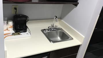 A compact kitchenette with a microwave, coffee maker, and sink.