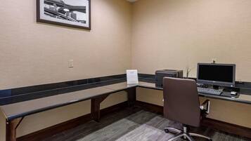 A hotel office with a desk, computer, chair, and a framed picture on the wall.