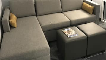 Un sofá seccional gris con un reposapiés a juego y una única almohada amarilla. Encima del sofá, hay tres cuadros enmarcados en la pared.