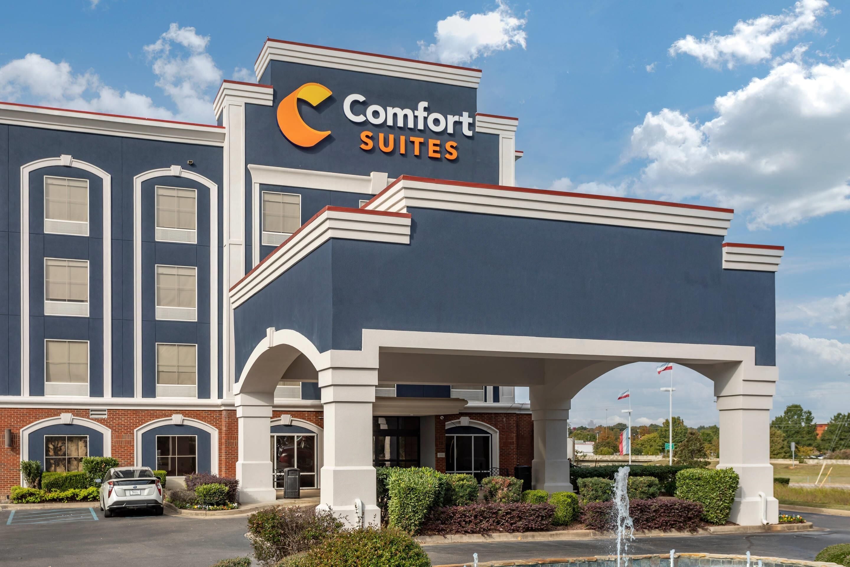 A hotel with a prominent 'Comfort Suites' sign, a brick facade, and a fountain in the entrance area.
