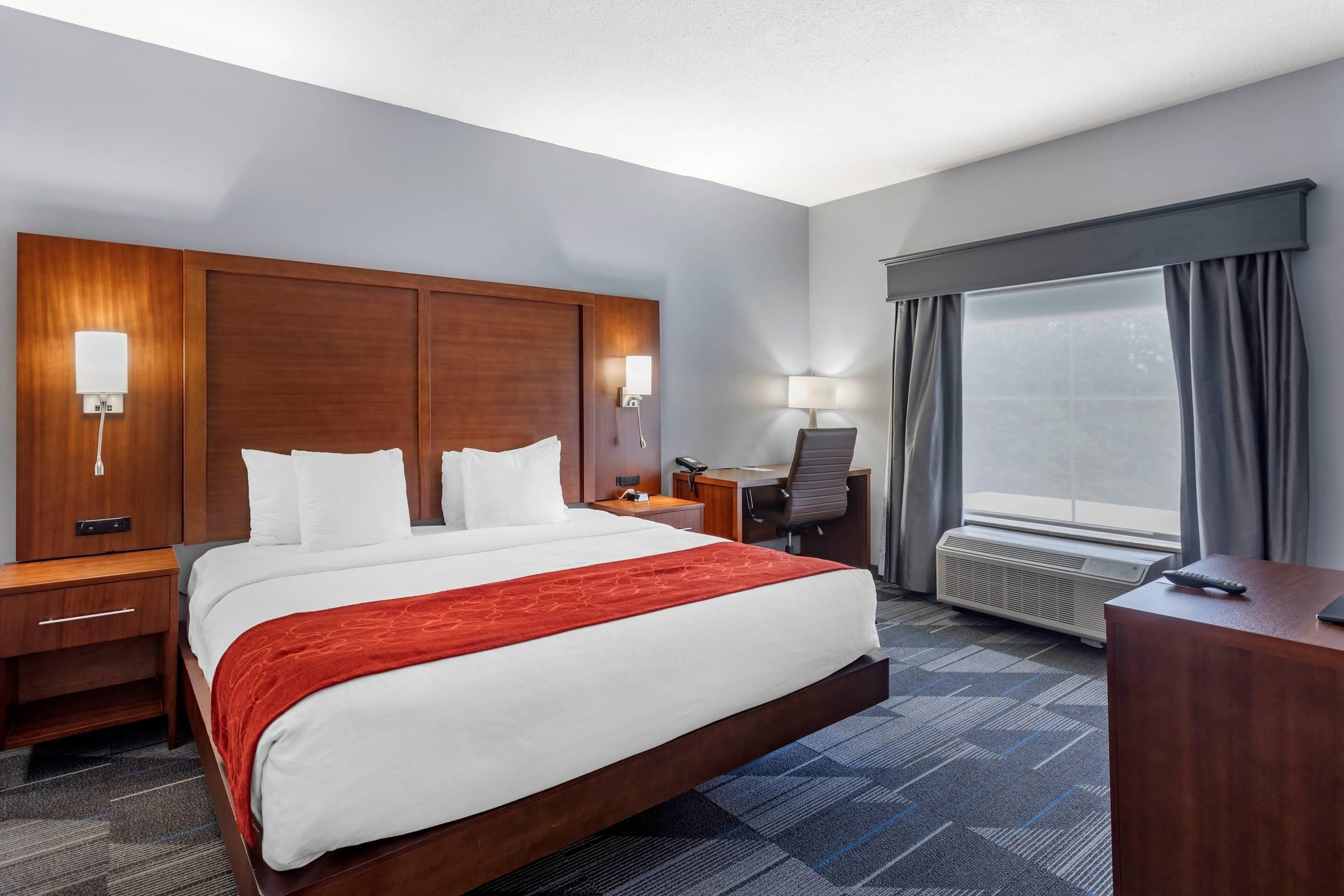 A hotel room with a large bed, bedside lamps, a desk, and a window with curtains.