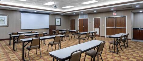 A conference room with tables, chairs, a projector screen, and a carpeted floor.